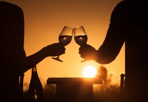 A couple toasts glasses of wine on a beach during their couples getaway